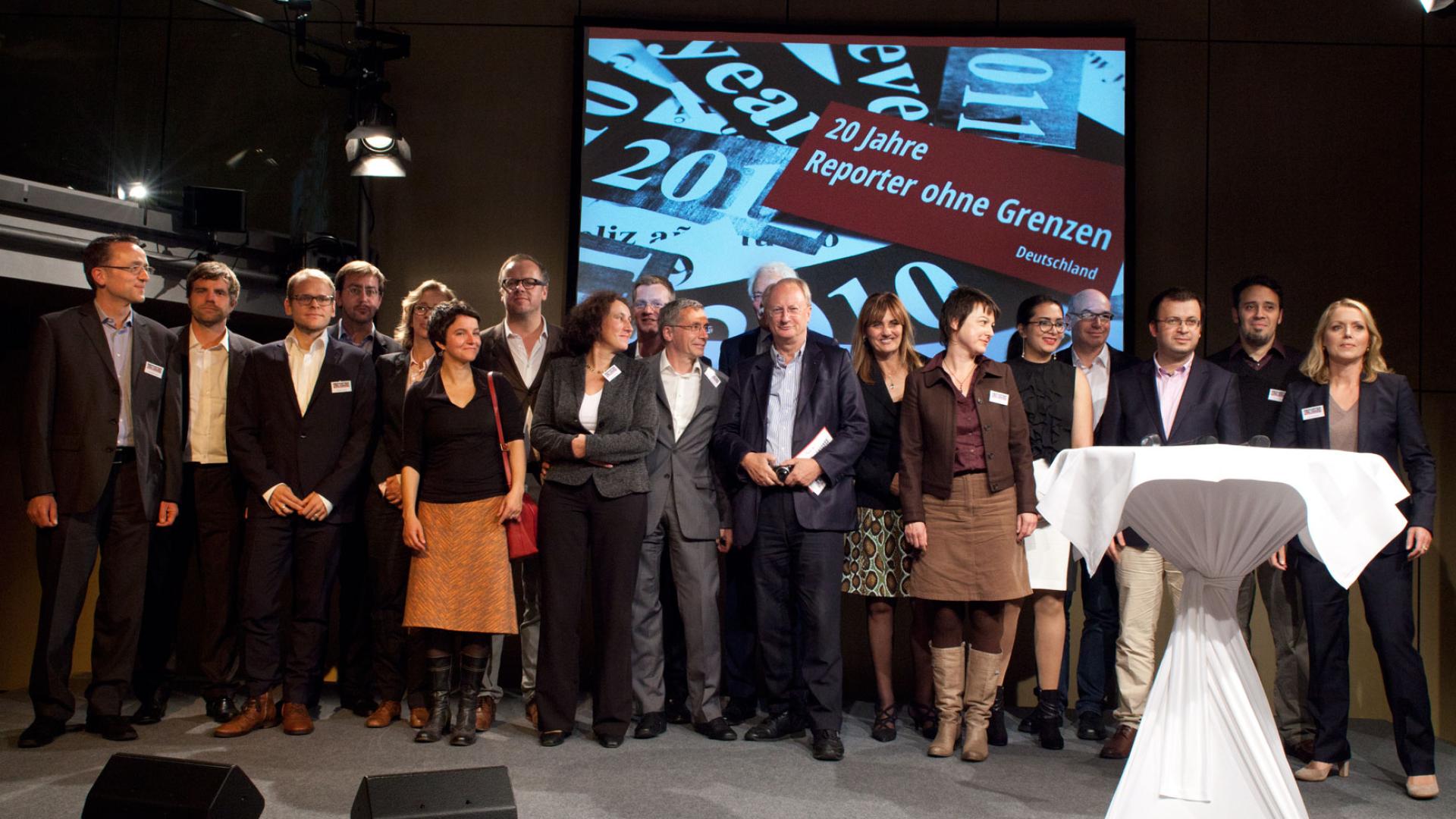 Eine Menschenmenge steht zur 20-Jahre-Veranstaltung in einem Raum zusammen. Hinter Ihnen ist ein Bild mit der Aufschrift "20 Jahre Reporter ohne Grenzen Deutschland" zu sehen