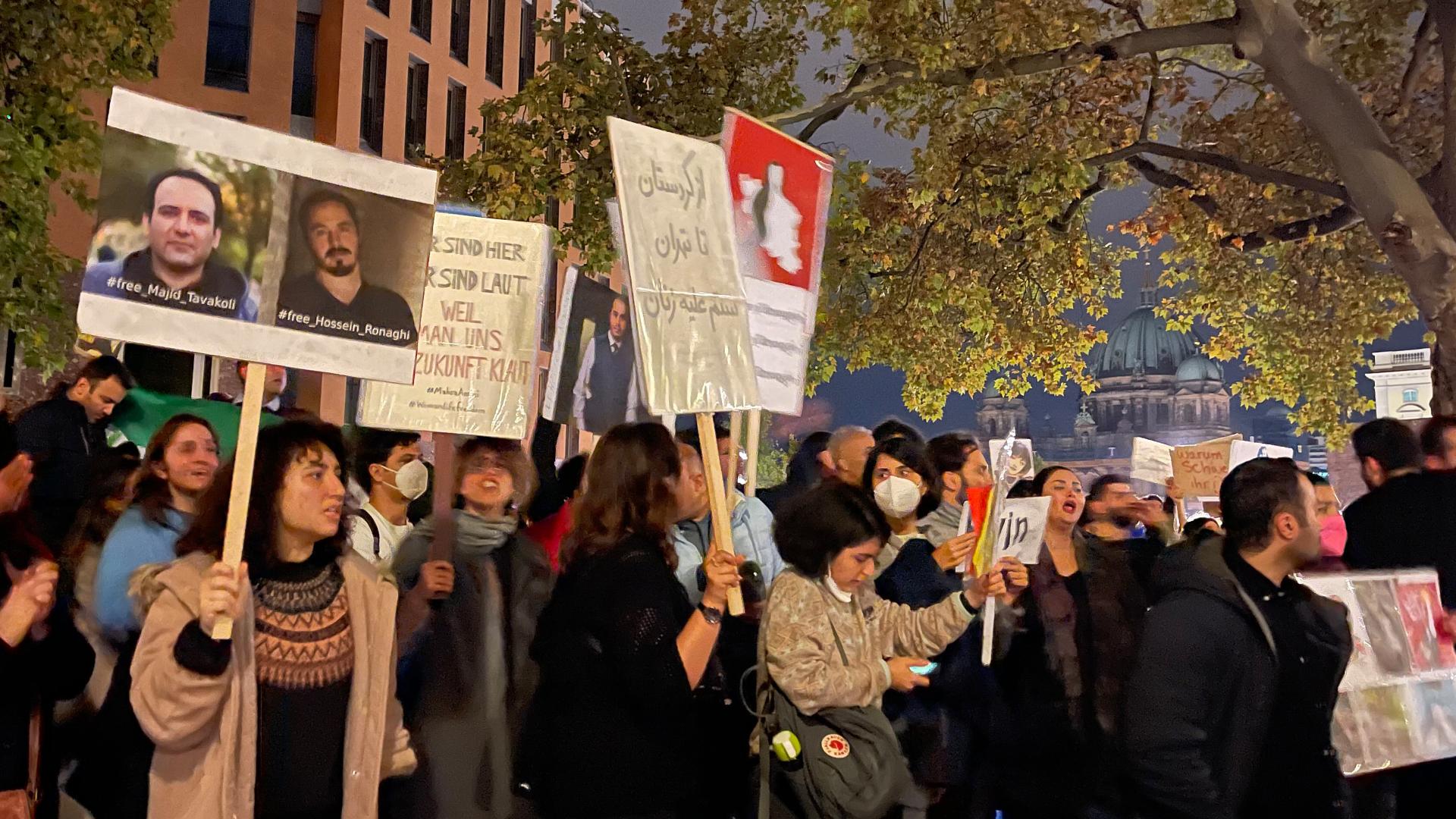 Menschen protestieren mit Schildern, auf denen Schriftzüge und Fotos von zwei Männern abgebildet sind.