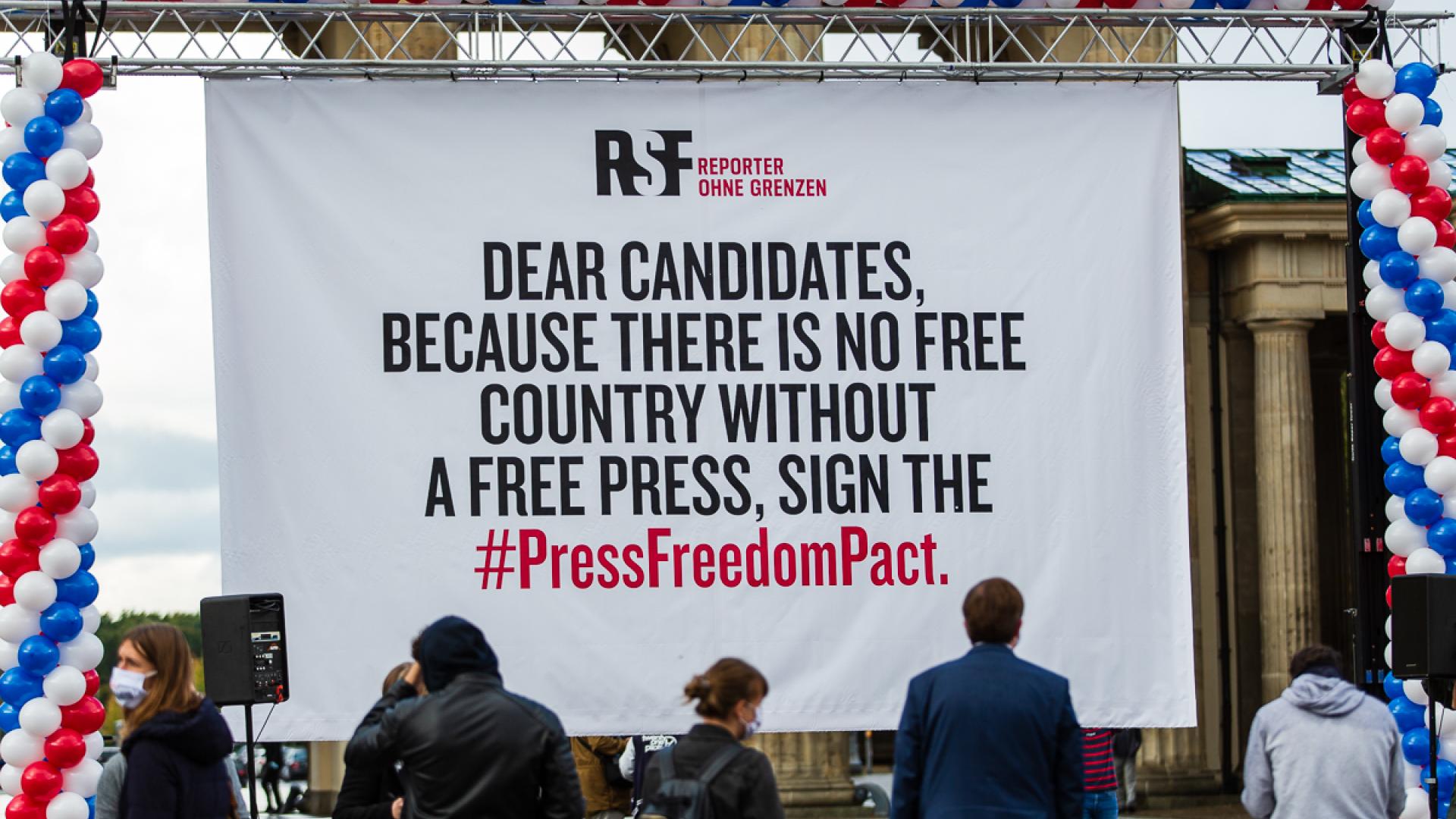 Ein großer weißer Banner mit der Aufschrift "Dear candidates, because there is no free country without a free press, sign the #PressFreedomPact." Rundherum blaue, weiße und rote Ballons.