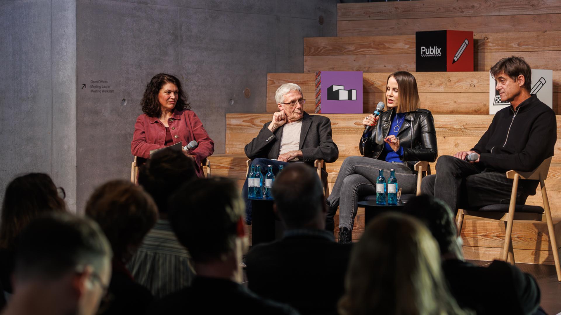 Zu sehen sind in einer geöffneten Runde sitzende Personen auf einer Bühne