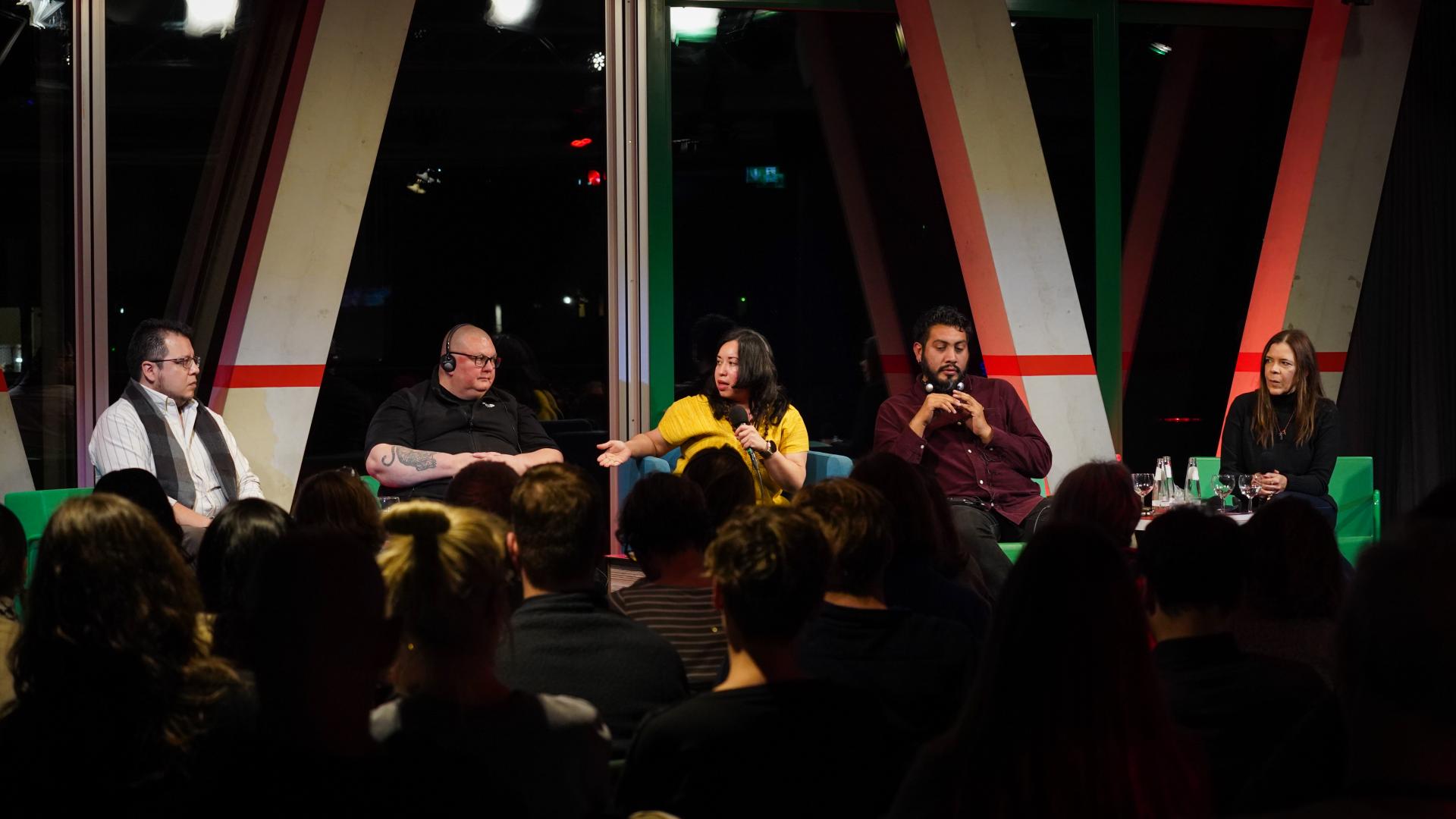 5 Personen sitzen auf einer Bühne vor einem großen Publikum