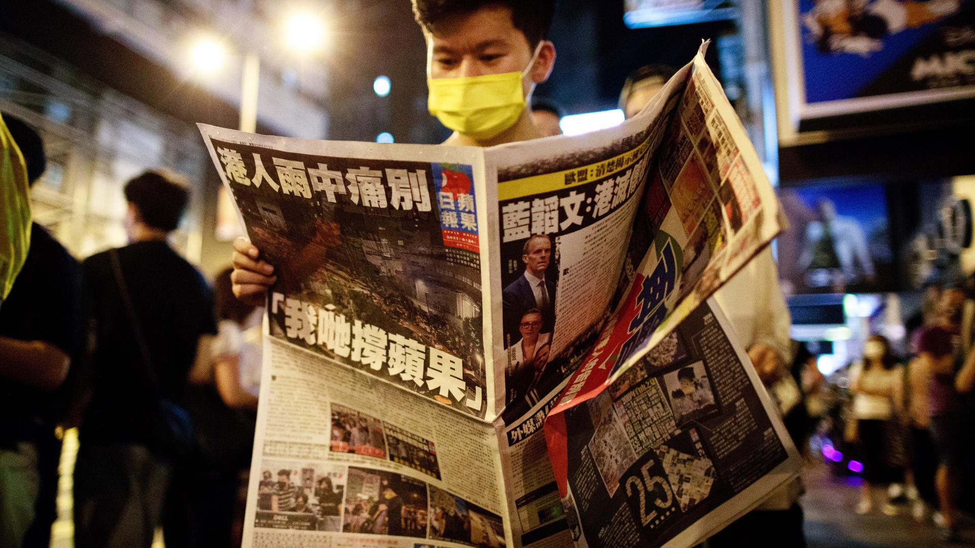 Ein Mann mit gelber Gesichtsmaske liest abends die letzte Ausgabe der Hongkonger Boulevard-Zeitung Apple Daily. 
