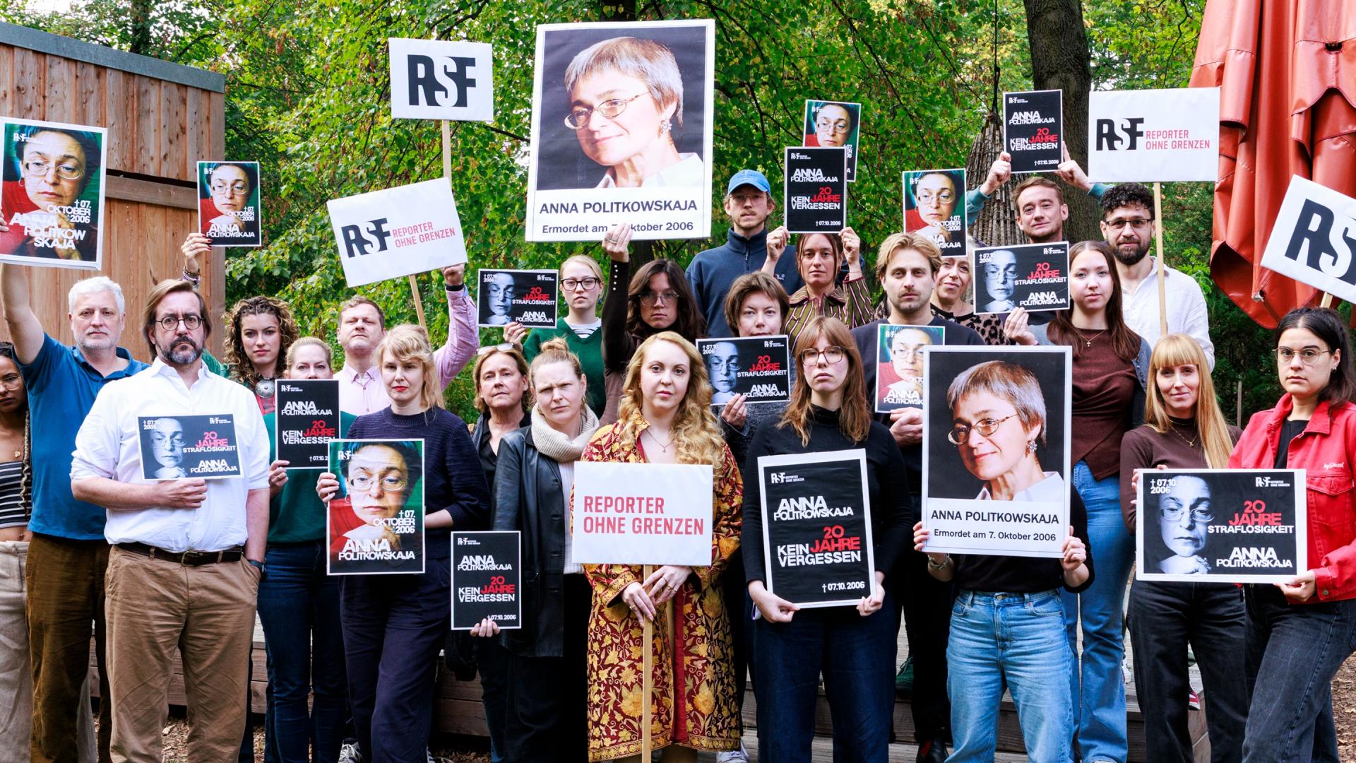 Eine große Gruppe an Menschen. Sie gucken ernst und halten Plakate mit Solidaritätsbotschaften für die ermordete Journalistin Anna Politkowskaja.